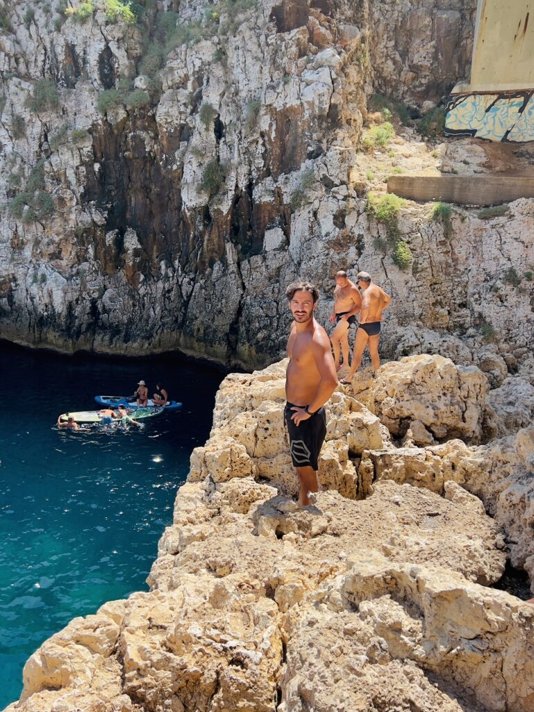 Jumping off the cliff at il Ciolo, Gagliano del Capo - one of Puglia’s most beautiful swimming spots, in a dramatic canyon underneath a bridge | Photo © the Puglia Guys for the Big Gay Podcast from Puglia guides to gay Puglia, Italy’s top gay summer destination